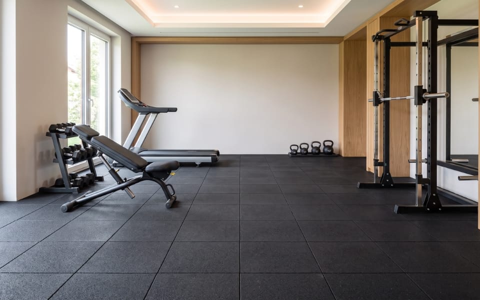 Black rubber tile flooring in a gym with a treadmill and a squat rack