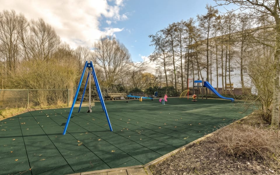Green safety tile surface around a swing frame in a park playground