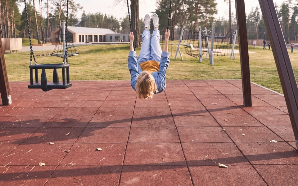 A child swinging above a red-brown safety tile surface