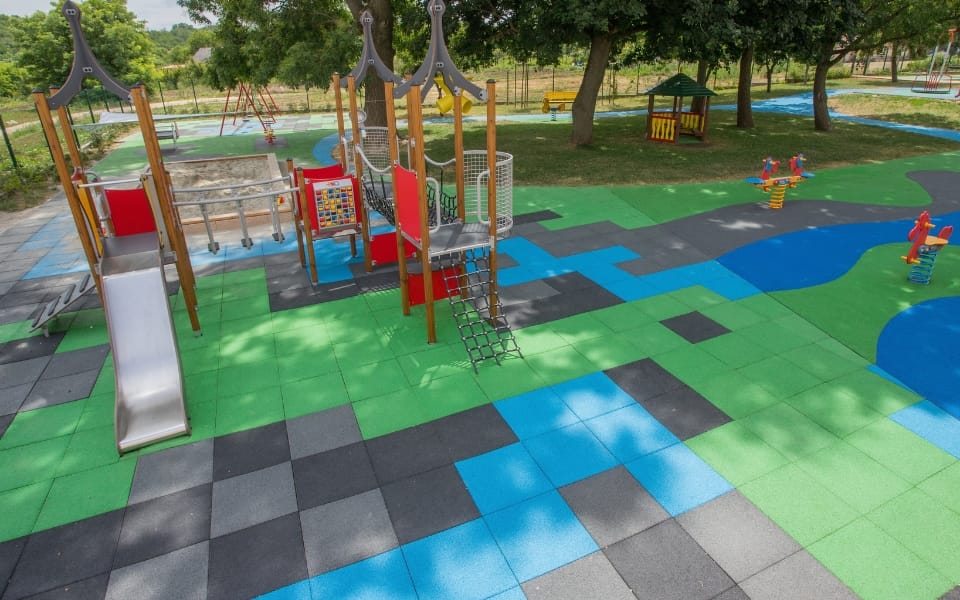 Colourful rubber safety tiles across a playground with climbing frames and springers