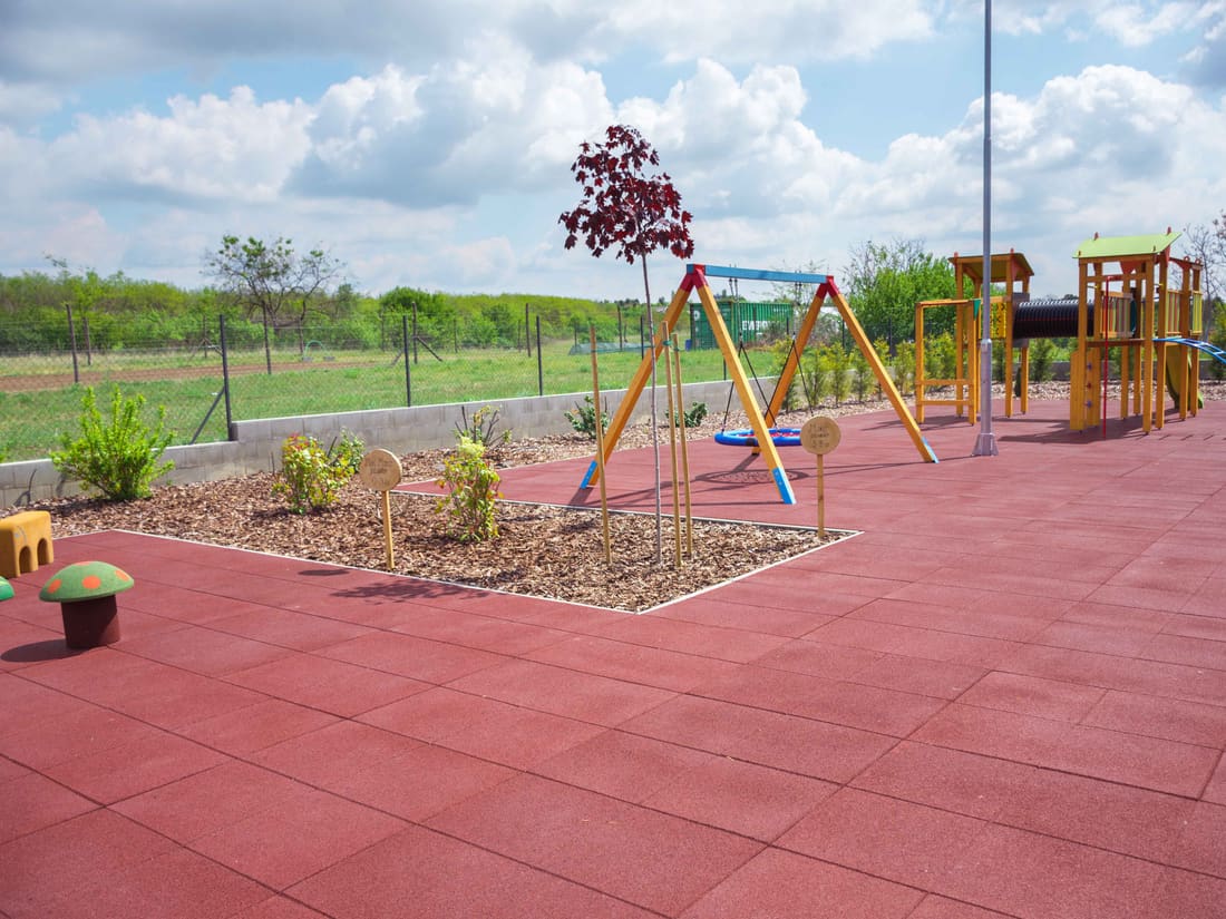 Playground with swings and a wooden play tower on red rubber tiles