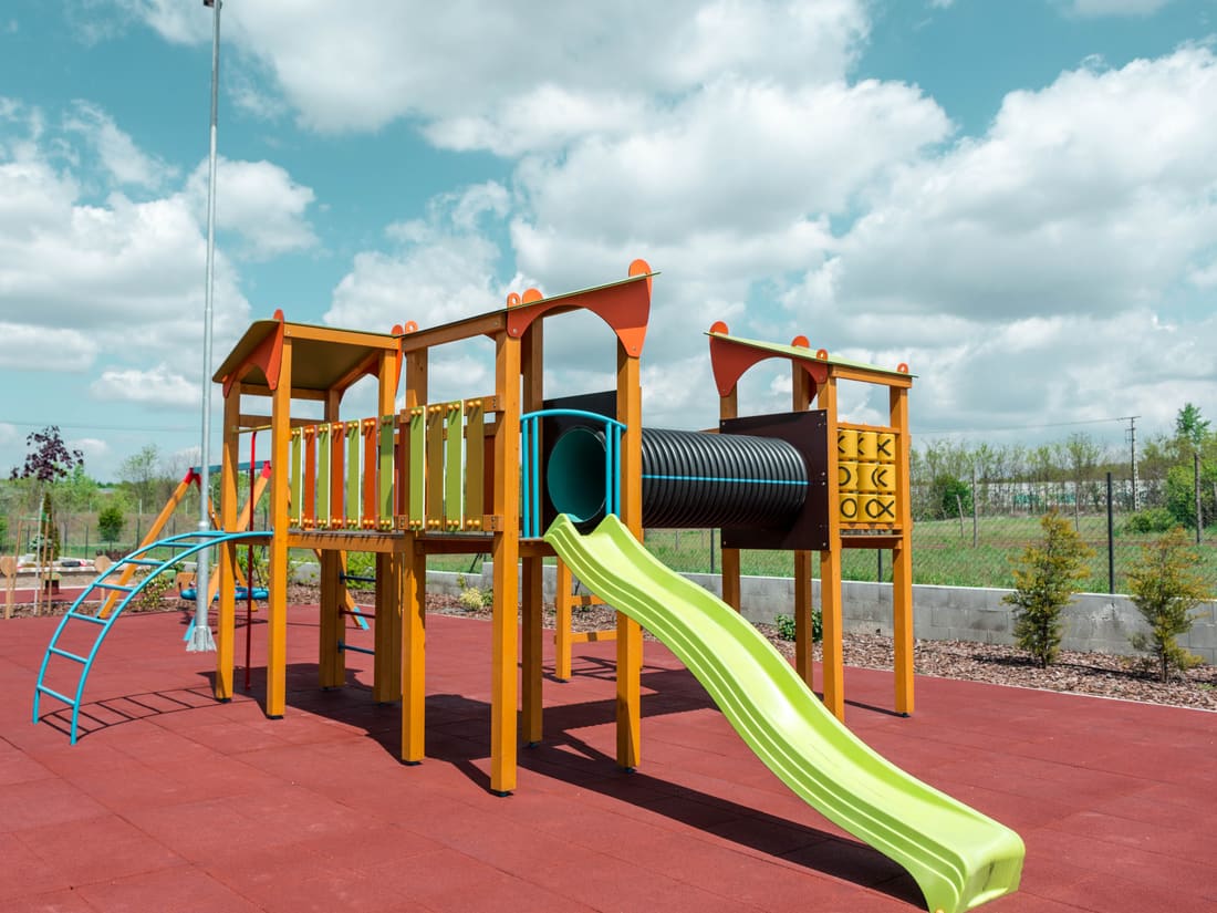 Wooden play tower with a green slide on red rubber tiles