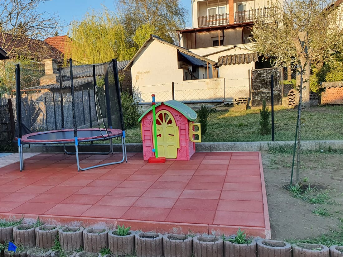 Trampoline and playhouse on red rubber tiles in a garden