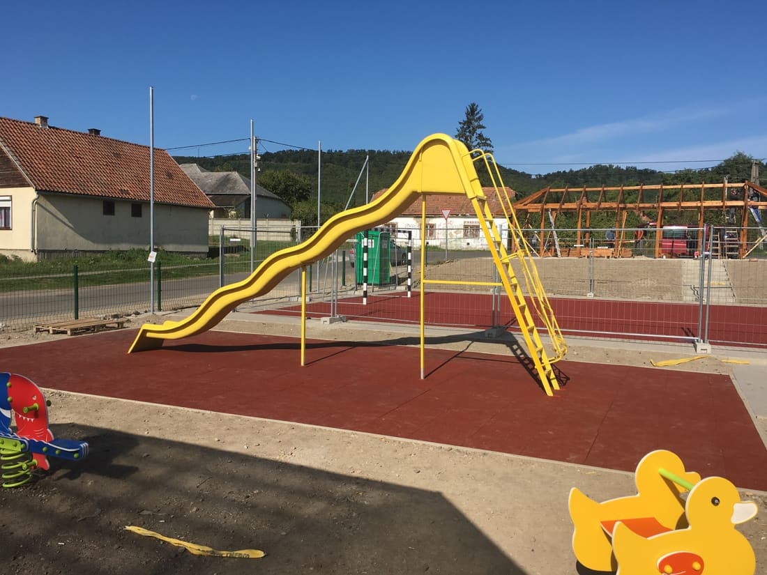 Yellow slide on red rubber tiles at the edge of the village