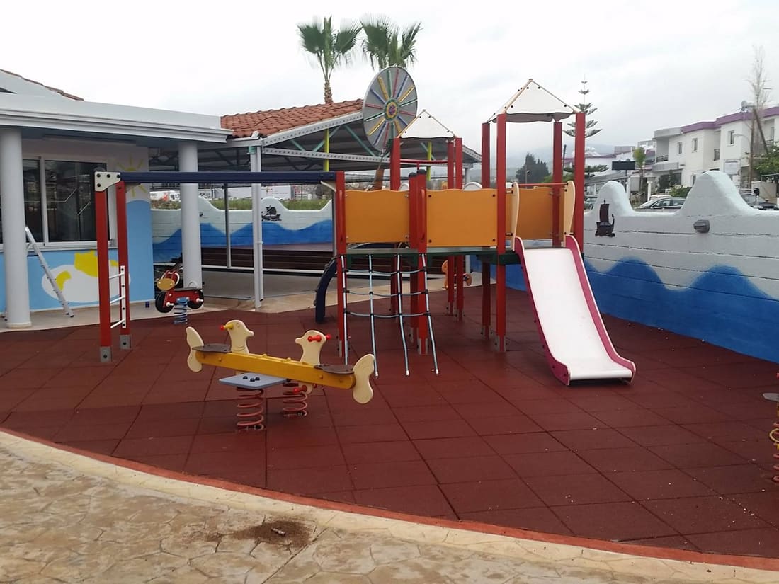 Colourful play equipment on red rubber tiles among palm trees