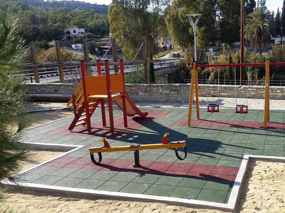 Seesaw on green and sand-coloured rubber tiles beside a sandpit