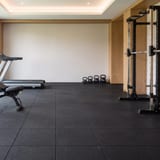 Black rubber tile flooring in a gym with a treadmill and a squat rack